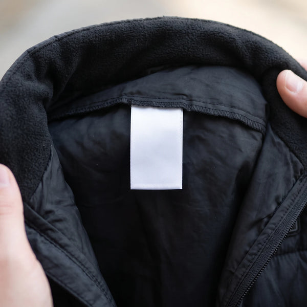 Two hands holding the vest collar open to show the sewn-in label