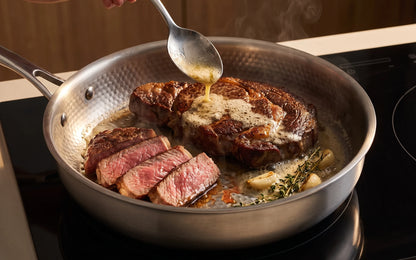 A steak with a dark seared crust in the hammered pan, butter spooned over it