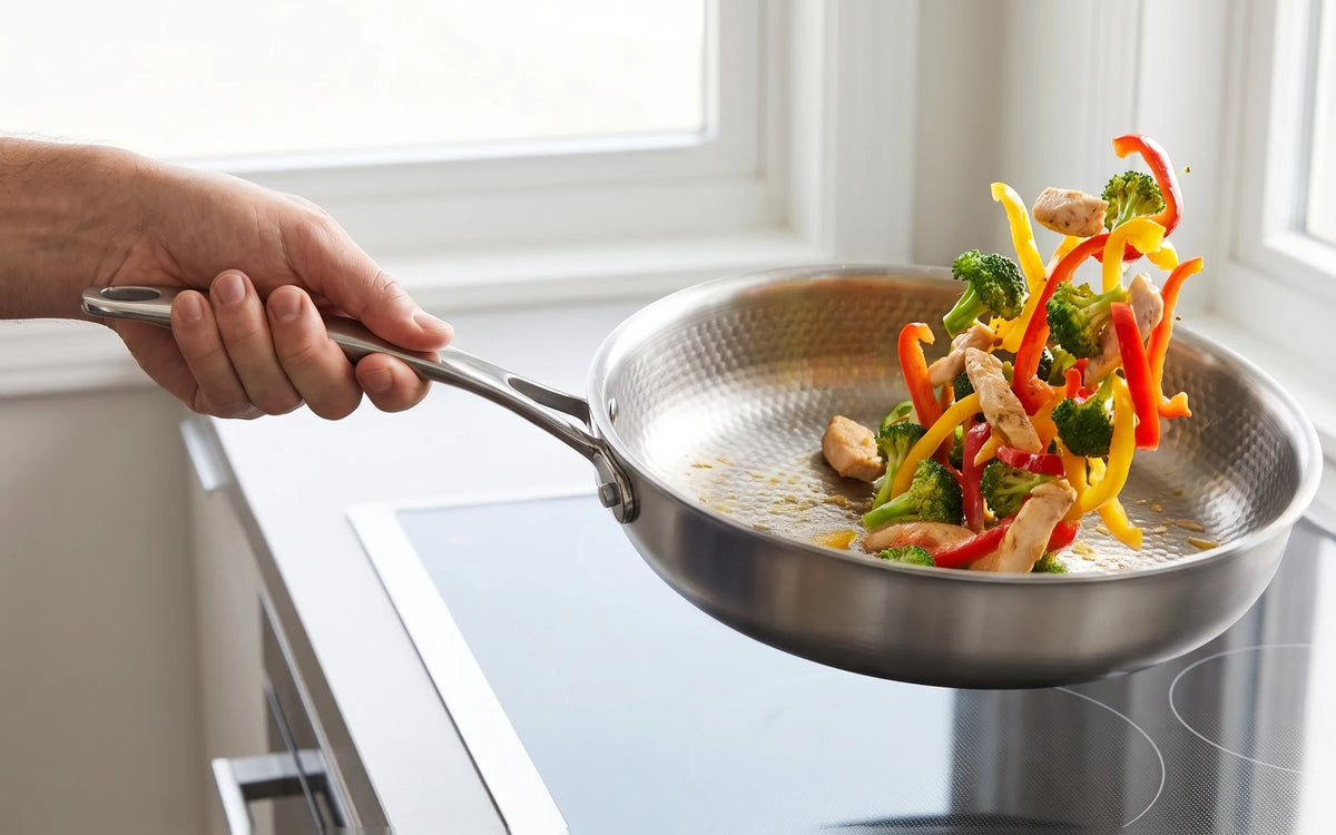 A hand tossing chicken, broccoli and peppers in the high-walled hammered pan